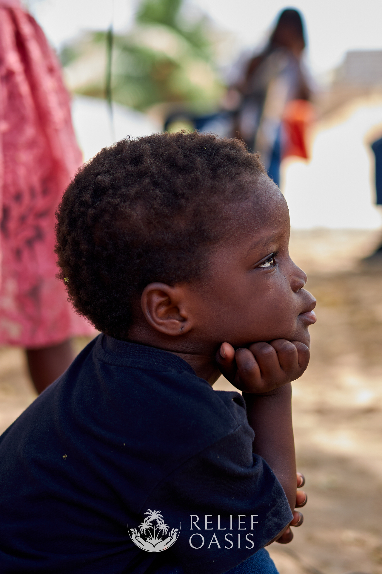 A young child resting their chin on their hand, gazing thoughtfully into the distance
